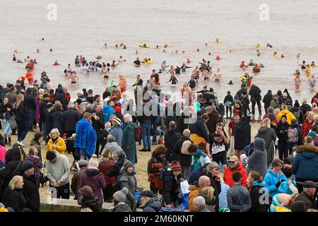 Lyme Regis, Dorset, Großbritannien. 1. Januar 2023 Hunderte von Neujahrsfeierern in schicken Kleidern, beobachtet von riesigen Menschenmassen, nehmen an einem bedeckten feuchten Tag am jährlichen Lyme Lunge-Schwimmen im Lyme Regis in Dorset Teil, um Mencap und der National Heart Foundation zu helfen. Bildnachweis: Graham Hunt/Alamy Live News Stockfoto