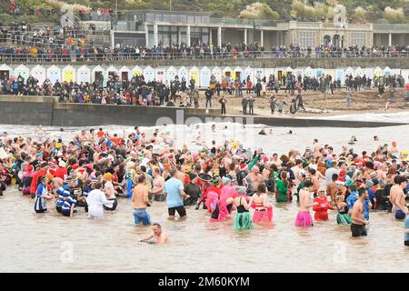 Lyme Regis, Dorset, Großbritannien. 1. Januar 2023 Hunderte von Neujahrsfeierern in schicken Kleidern, beobachtet von riesigen Menschenmassen, nehmen an einem bedeckten feuchten Tag am jährlichen Lyme Lunge-Schwimmen im Lyme Regis in Dorset Teil, um Mencap und der National Heart Foundation zu helfen. Bildnachweis: Graham Hunt/Alamy Live News Stockfoto