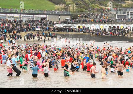 Lyme Regis, Dorset, Großbritannien. 1. Januar 2023 Hunderte von Neujahrsfeierern in schicken Kleidern, beobachtet von riesigen Menschenmassen, nehmen an einem bedeckten feuchten Tag am jährlichen Lyme Lunge-Schwimmen im Lyme Regis in Dorset Teil, um Mencap und der National Heart Foundation zu helfen. Bildnachweis: Graham Hunt/Alamy Live News Stockfoto