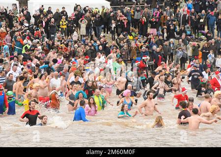 Lyme Regis, Dorset, Großbritannien. 1. Januar 2023 Hunderte von Neujahrsfeierern in schicken Kleidern, beobachtet von riesigen Menschenmassen, nehmen an einem bedeckten feuchten Tag am jährlichen Lyme Lunge-Schwimmen im Lyme Regis in Dorset Teil, um Mencap und der National Heart Foundation zu helfen. Bildnachweis: Graham Hunt/Alamy Live News Stockfoto