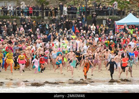 Lyme Regis, Dorset, Großbritannien. 1. Januar 2023 Hunderte von Neujahrsfeierern in schicken Kleidern, beobachtet von riesigen Menschenmassen, nehmen an einem bedeckten feuchten Tag am jährlichen Lyme Lunge-Schwimmen im Lyme Regis in Dorset Teil, um Mencap und der National Heart Foundation zu helfen. Bildnachweis: Graham Hunt/Alamy Live News Stockfoto