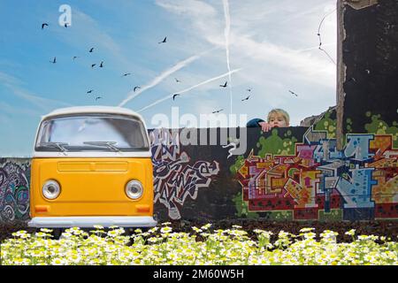 Ein kleiner Junge klettert an die Wand, um das gelbe alte Auto zu sehen, das vor einer Graffiti-Wand geparkt ist Stockfoto