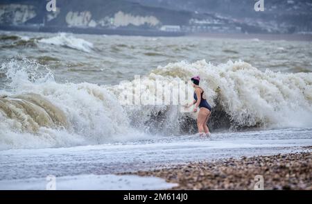 Seaford, Großbritannien. 1. Januar 2023. Wetter im Vereinigten Königreich: Schwimmer feiern den Neujahrstag, indem sie die stürmischen Meere in Seaford in East Sussex, Großbritannien, mutig testen. Kredit: Jim Holden/Alamy Live News Stockfoto