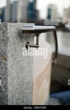 Handgeländer aus Metall mit Wassertropfen an grauem Marmorblock in städtischer Umgebung mit unscharfen Hintergrundbildern Stockfoto