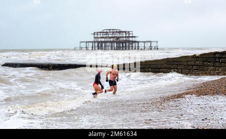 Brighton UK 1. Januar 2023 - Schwimmer am Neujahrstag tauchen in Brighton in der Nähe des West Pier bei düsterem bewölktem Wetter ins Meer ein : Credit Simon Dack / Alamy Live News Stockfoto