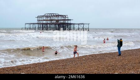 Brighton UK 1. Januar 2023 - Schwimmer am Neujahrstag tauchen in Brighton in der Nähe des West Pier bei düsterem bewölktem Wetter ins Meer ein : Credit Simon Dack / Alamy Live News Stockfoto