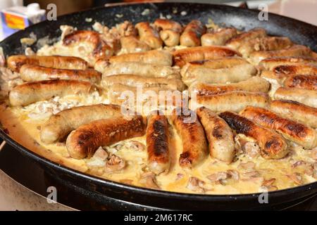 Bratwürste in einer großen Pfanne mit Pilzen und Weiße Sauce auf dem Markt in Paris Stockfoto