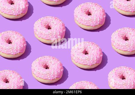 Pinkfarbenes Donuts-Muster auf lila Hintergrund. Trendige sommerliche Ästhetik im Hintergrund. Lebendige Farben. Süße Speisen - visuelles Konzept. Stockfoto