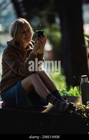 Eine Frau sitzt im Park mit einer Tasse Mate. Stockfoto