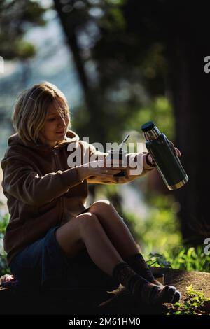 Eine Frau sitzt im Park mit einer Thermoskanne und einer Tasse Mate. Stockfoto