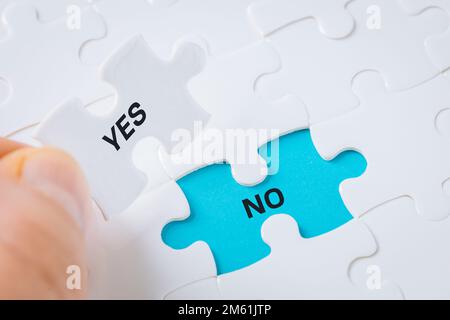 Ja, nein, die weiße Puzzle-Hand nimmt das Wort "Ja" auf und enthüllt das Wort "Nein" auf blauem Hintergrund, Konzept, Zustimmung und Ablehnung und trifft eine Entscheidung Stockfoto