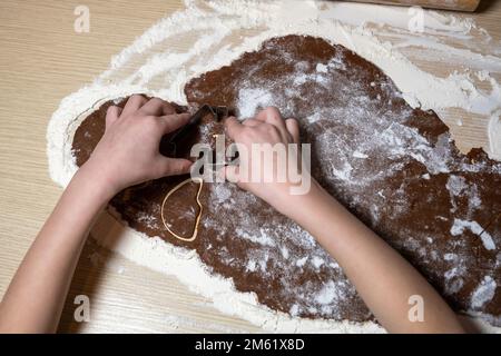 Nahaufnahme von Kinderhänden, die Lebkuchenform schnitzen. Weihnachtskonzept. Stockfoto