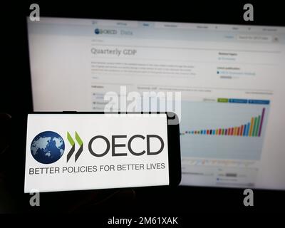 Person, die ein Smartphone mit dem Logo der zwischenstaatlichen Organisation OECD auf dem Bildschirm vor der Website hält. Konzentrieren Sie sich auf das Display des Telefons. Stockfoto