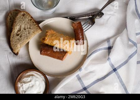 Gefüllte Kohlbrötchen mit Fleisch und Würstchen auf einem Teller mit Scheiben Brot und saurer Sahne. Stockfoto