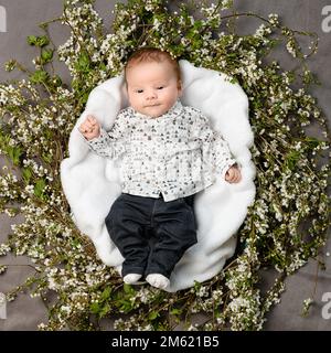 Rivne, Ukraine 25. April 2022: Ein neugeborener Junge liegt im Kreis mit Blumen auf grauem Hintergrund, der Junge liegt auf einer weißen Windel mit Blumen. Stockfoto