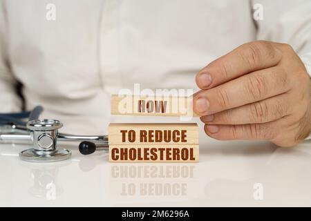 Medizinisches Konzept. Auf einer weißen Oberfläche, einem Stethoskop und Holzplatten mit der Beschriftung - so reduzieren Sie Cholesterin Stockfoto