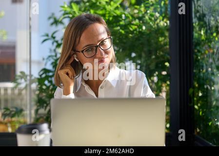 Junge Frau, die ein Videogespräch mit einem Laptop führt. Glückliche Geschäftsfrau, die ein virtuelles Meeting mit einem Kunden in einem Café hat Stockfoto