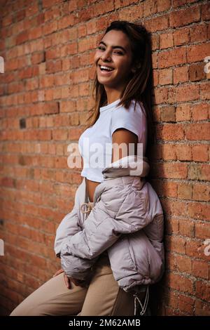 Marokkanische Frau, die in die Kamera schaut und lacht, während sie sich gegen eine Mauer lehnt. Stockfoto