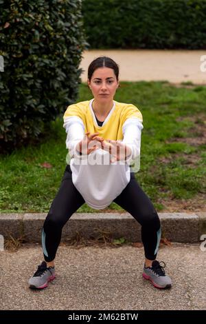Von oben: Junge Sportlerin in Sportbekleidung, die im Park Squats macht Stockfoto