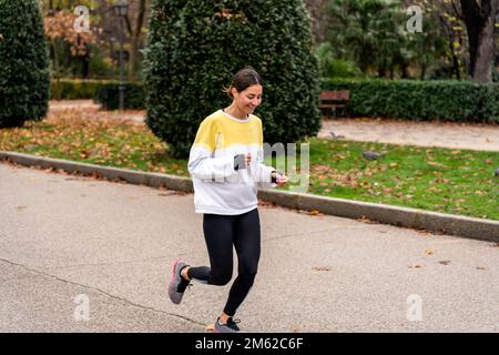 Fröhliche junge Frau in Aktivkleidung und Turnschuhe, die auf dem Weg laufen, während sie im Green Park trainieren Stockfoto