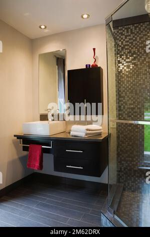 Glasdusche und schwarze Holzschränke und weißes quadratisches Porzellanwaschbecken im Badezimmer im luxuriösen Haus. Stockfoto