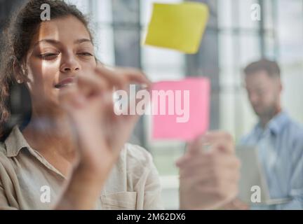 Ihre Vision zum Leben erwecken. Aufnahme einer selbstbewussten Geschäftsfrau, die ihrem Kollegen mit Haftnotizen an einer Glaswand im Büro eine Idee vorstellt. Stockfoto