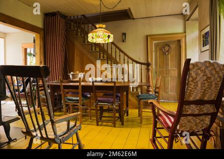 Antike Holzschaukelstühle und langer brauner Esstisch aus Holz mit Stühlen im Speisesaal im alten 1838 Canadiana Feldsteinhaus. Stockfoto