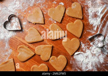 Herzkekse, Teig und Schimmelpilze auf dem Tisch mit Mehl. Valentinstag-Feier. Selbst gebacken. Stockfoto