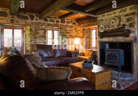 Braune Ledersofas mit hölzernem Kofferraum Couchtisch und Holzofen im Kamin im Wohnzimmer im alten, ca. 1850 Jahre alten Feldsteinhaus. Stockfoto