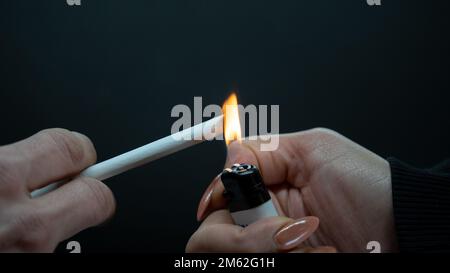 Ein Mann mit einer Zigarette auf schwarzem Hintergrund. Brennende Zigarette mit Feuerzeug Stockfoto