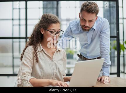 Eine Geschäftsfrau, die mit ihrem Kollegen im Büro auf ein Notebook schaut Stockfoto