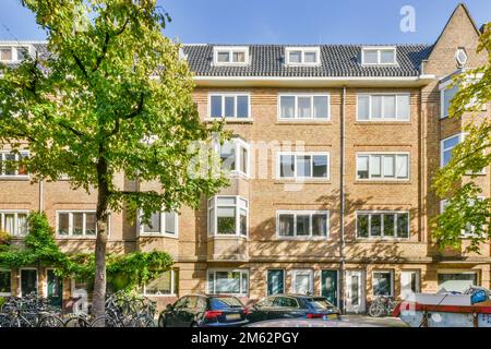 Ein Apartmentkomplex in den niederlanden mit Fahrrädern, die auf der Straße geparkt sind, und Autos, die entlang der befahrenen Straße geparkt werden Stockfoto