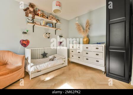 Ein Kinderzimmer mit Möbeln und Spielzeug an der Wand, einschließlich eines Babykribetts in einem weißen Bett Stockfoto