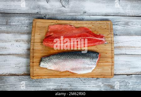 Zwei Filets, mit der Schale nach oben und unten, mit Lachs auf dem Schneidebrett mit weißem rustikalem Holztisch Stockfoto