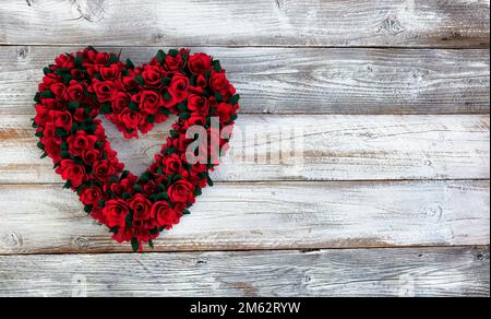 Großer hölzerner Herzkranz aus kleinen roten Rosenblumen auf weißem rustikalem Holz für ein glückliches Valentinstag-Konzept mit Kopierbereich Stockfoto