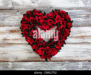 Großer hölzerner Herzkranz mit kleinen roten Rosenblumen auf weißem rustikalem Holz für ein fröhliches Valentinstag-Konzept Stockfoto