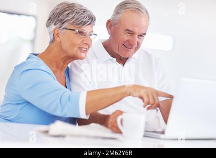 Paar mit Laptop. Lächelnder erwachsener Mann, der ein Notebook benutzt, während eine Frau auf den Bildschirm zeigt. Stockfoto