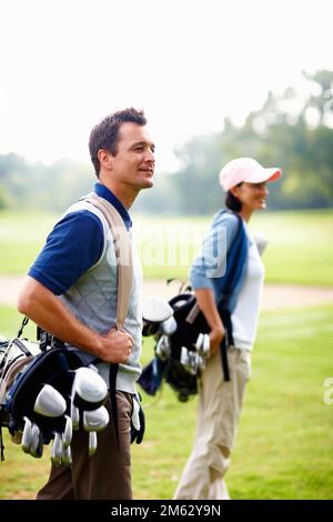 Mann und Frau mit Golftaschen. Mann und Frau, die Golftaschen tragen und wegschauen. Stockfoto