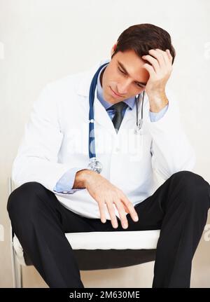 Überarbeiteter Arzt mit Hand am Kopf, gestresst. Porträt eines überarbeiteten Arztes mit Hand an Kopf, der total gestresst aussah. Stockfoto