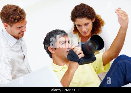 Fotografen, die Fotos in der Kamera auschecken. Fotograf mittleren Alters, der seinen Kollegen Fotos in seiner Kamera zeigt. Stockfoto