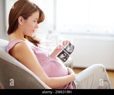 Ich kann es kaum erwarten, Sie kennenzulernen... Eine wunderschöne schwangere Frau, die sich Ultraschallbilder ihres Babys ansieht - Copyspace. Stockfoto