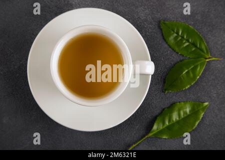 Teeblätter mit einer Tasse grünem Tee auf schwarzem Hintergrund Stockfoto