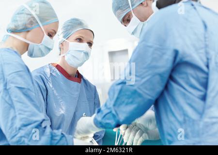 Lassen Sie sich für die beste medizinische Versorgung absichern. Vielfältige Gruppe von Chirurgen, die als Team an einem Patienten in der Notaufnahme arbeiten. Stockfoto