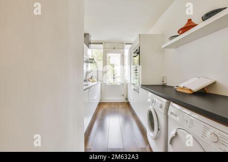 Ein Waschraum mit Holzfußboden und einer weißen Waschmaschine in der Gegend ist gut beleuchtet durch natürliches Licht vom Fenster Stockfoto