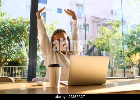 Erschöpfte Geschäftsfrau, die sich mit erhobenen Armen streckt, während sie in einer Arbeitsstelle arbeitet. Stockfoto