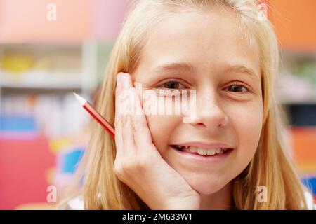 Schulen sind ein Kinderspiel, wenn man gerne lernt. Süßes Schulmädchen, das mit einem Bleistift in der Hand in die Kamera lächelt - Kopierraum. Stockfoto