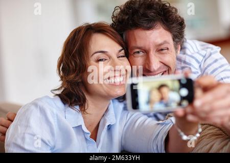 Teilen wir unsere Liebe mit allen. Ein Mann und seine Frau machen zu Hause ein Selfie. Stockfoto