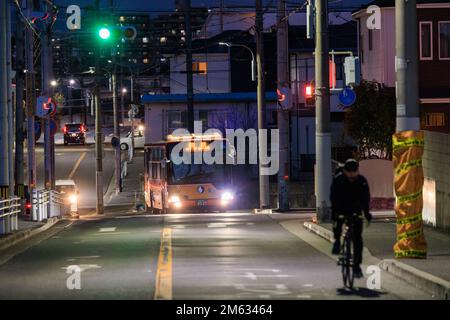 Akashi, Japan - 29. Dezember 2022: Radfahrer fahren auf einer Vorstadtstraße, während der Bus nachts näher kommt Stockfoto