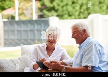 Unser Enkel hat heute seine ersten Schritte unternommen. Ein älteres Paar, das ein Tablet benutzt, während es auf seiner Terrasse sitzt. Stockfoto