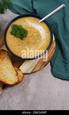 Rote Linsen Suppenpüree in dunkler Schüssel mit Brot auf grauem Marmortisch Stockfoto
